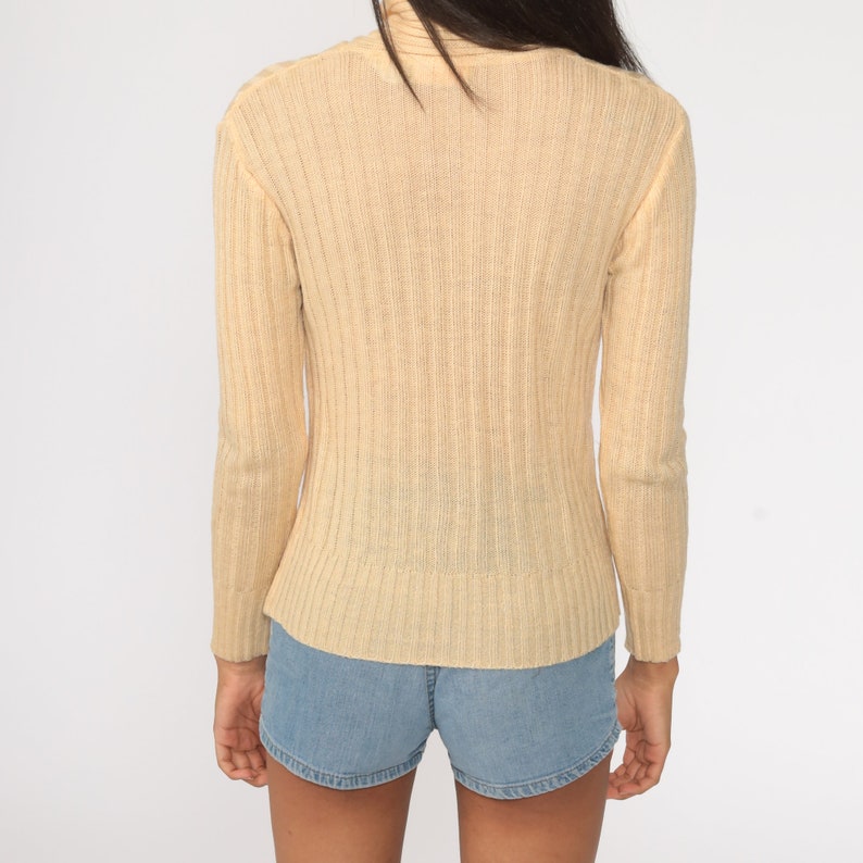 May include: A cream-colored ribbed knit sweater with long sleeves and a turtleneck.