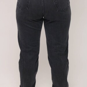 May include: Dark gray Wrangler jeans with a classic five-pocket design. The jeans have a straight leg fit and a Wrangler brand patch on the back pocket. The denim appears to be pre-worn.