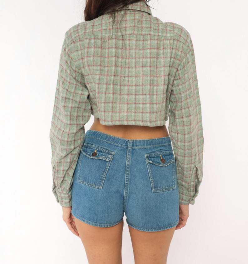 Puede incluir: Una camisa corta de manga larga con un patr&oacute;n de cuadros en verde claro y rojo, combinada con pantalones cortos de mezclilla azul que incluyen dos bolsillos traseros con solapas abotonadas. La camisa tiene cuello y pu&ntilde;os abotonados.