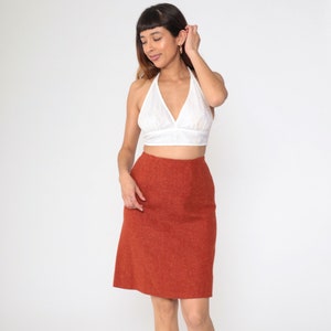 May include: A white halter top with a V-neck and a rust-colored knee-length skirt. The skirt has a straight cut and a textured appearance. The outfit is suitable for casual or semi-formal occasions.