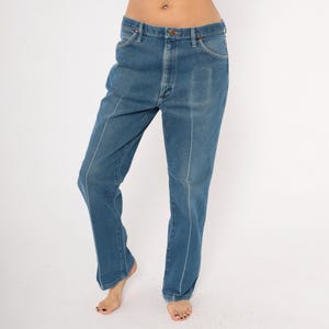 Peut inclure: Jean en denim bleu avec une coupe droite. Le jean a une conception classique &agrave; cinq poches et une fermeture &agrave; bouton et fermeture &eacute;clair. Des coutures blanches accentuent les coutures et les poches. Le jean est port&eacute; par une personne.