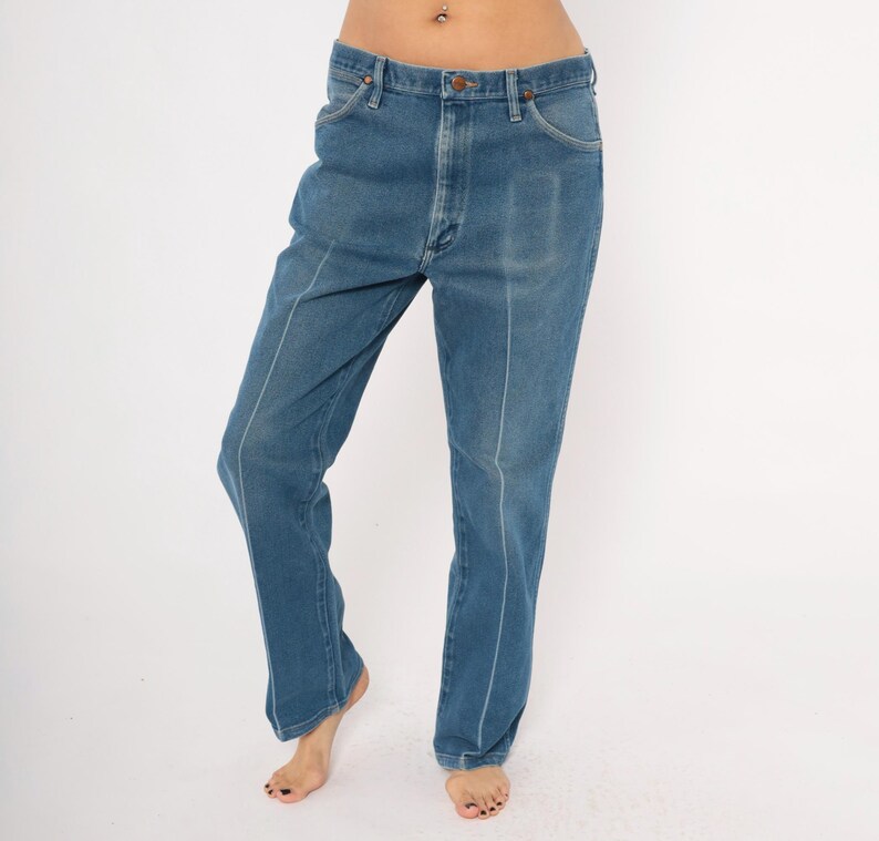 Peut inclure: Jean en denim bleu avec une coupe droite. Le jean a une conception classique &agrave; cinq poches et une fermeture &agrave; bouton et fermeture &eacute;clair. Des coutures blanches accentuent les coutures et les poches. Le jean est port&eacute; par une personne.