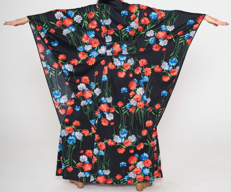May include: A black maxi dress with a floral print featuring red, blue, and white flowers. The dress has a wide, flowing silhouette and a long, flowing skirt.