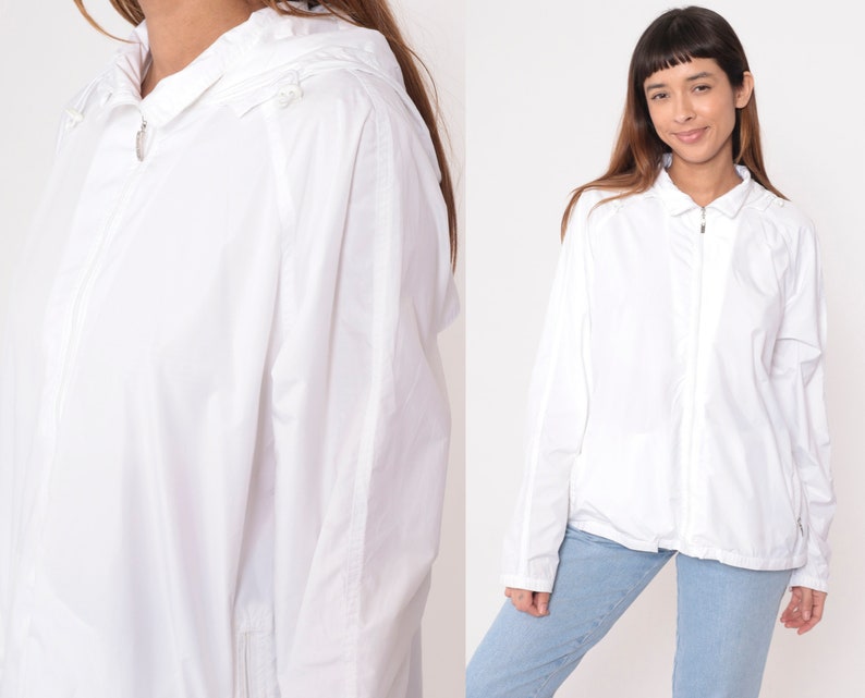 May include: White hooded jacket with a full-length zipper closure. The jacket has long sleeves and a collared neckline. The fabric appears lightweight and suitable for layering. The jacket is shown on a person wearing blue jeans.