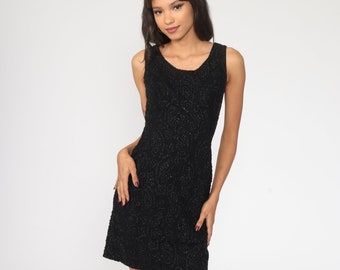May include: A black sleeveless dress with a sparkly, textured fabric. The dress has a scoop neckline and a fitted silhouette.
