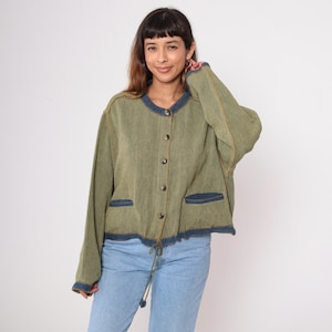 May include: Olive green jacket with a round neckline, button closure, and two front pockets. The jacket has denim blue trim on the collar, pockets, and cuffs. The jacket has a drawstring at the waist. The model is wearing light blue jeans.