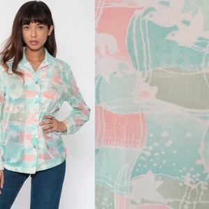 Puede incluir: Una camisa abotonada con un estampado abstracto en tonos pastel en azul claro, rosa y verde. La camisa de manga larga tiene cuello y est&aacute; hecha de una tela ligera y semitransparente.