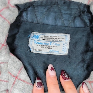 Puede incluir: Una camisa gris con un patr&oacute;n de cuadr&iacute;cula roja y un forro interior acolchado de color azul oscuro. Una etiqueta rectangular blanca est&aacute; cosida en el &aacute;rea del cuello, con el texto Towncraft Plus, 90% lana reprocesada, 10% nailon.