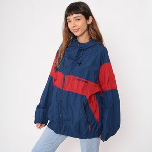 May include: A blue and red windbreaker jacket with a zipper closure and a hood. The jacket has the word "HEAD" embroidered on the front in white.