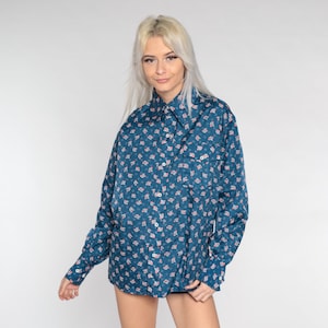 May include: A teal blue long-sleeved shirt with a white and pink floral pattern. The shirt has a collared neckline and a button-up front.