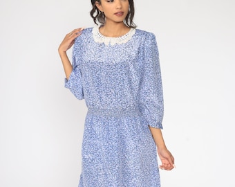 Könnte beinhalten: Hellblaues Kleid mit Blumenmuster und weißem Spitzenkragen. Das Kleid hat Dreiviertelärmel und eine geraffte Taille. Der Rock reicht bis zur Mitte des Oberschenkels. Das Kleid ist aus leichtem Stoff gefertigt.
