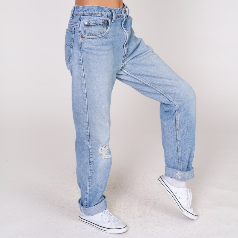 May include: A pair of light blue denim jeans with a distressed look. The jeans are cuffed at the ankles and have a relaxed fit.