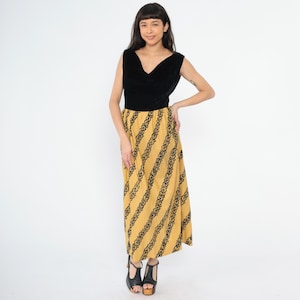 May include: A long black velvet and yellow patterned sleeveless dress. The dress has a V-neckline and a fitted bodice. The skirt is full and flows to the floor.