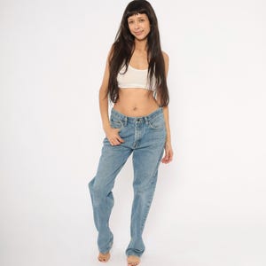 Peut inclure: Jean bleu clair en denim avec une conception classique &agrave; cinq poches. Le jean a une coupe droite et une fermeture &agrave; bouton et fermeture &eacute;clair. Le mod&egrave;le porte un crop top blanc. Le fond est blanc.