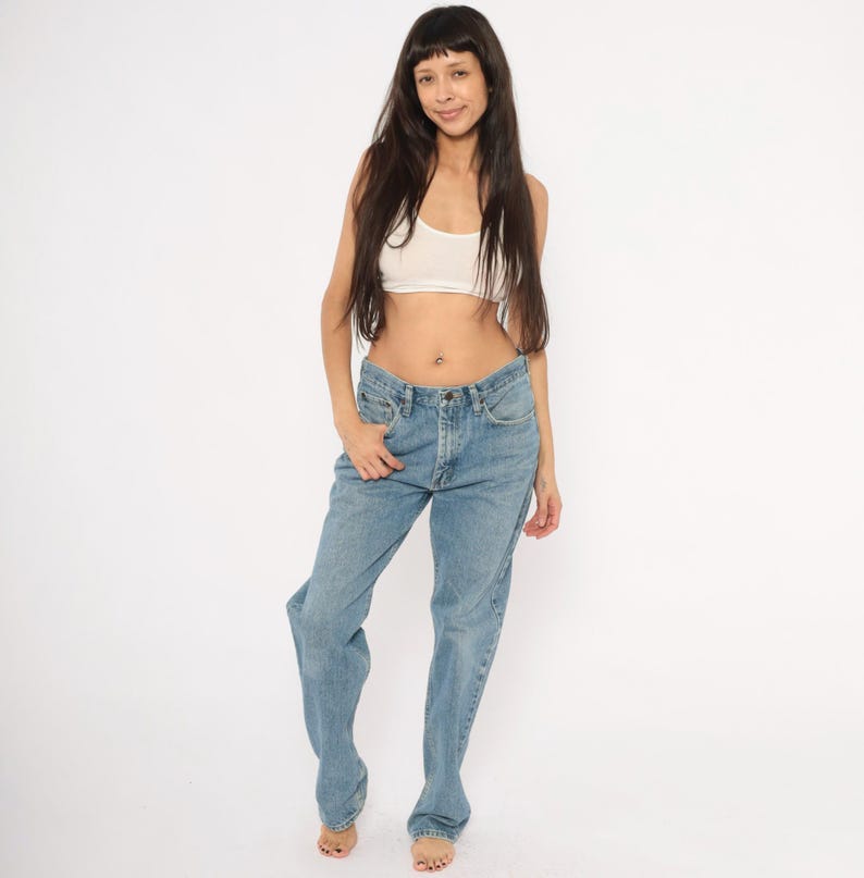 Peut inclure: Jean bleu clair en denim avec une conception classique &agrave; cinq poches. Le jean a une coupe droite et une fermeture &agrave; bouton et fermeture &eacute;clair. Le mod&egrave;le porte un crop top blanc. Le fond est blanc.