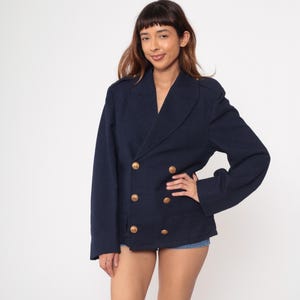 May include: A navy blue double-breasted blazer with gold-colored buttons. The blazer has a classic design with a notched collar and shoulder epaulettes. The jacket is a medium weight and appears to be made of a wool blend.