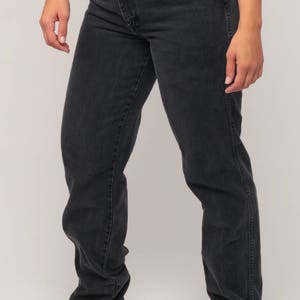 May include: Dark gray denim jeans with a classic five-pocket design. The jeans have a straight leg fit and a button and zipper closure. The front pockets have a contrasting dark blue fabric. The model is wearing the jeans.