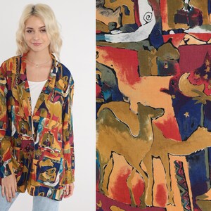 May include: A colorful, open-front blazer with a vibrant abstract pattern in shades of yellow, red, blue, and brown. The blazer features a classic lapel and two front pockets. The fabric design includes camel figures and architectural shapes.