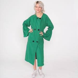 May include: A long, emerald green coat with a wrap-style front and large black buttons. The coat features wide sleeves with a flared design at the wrists. The model is wearing white sneakers.