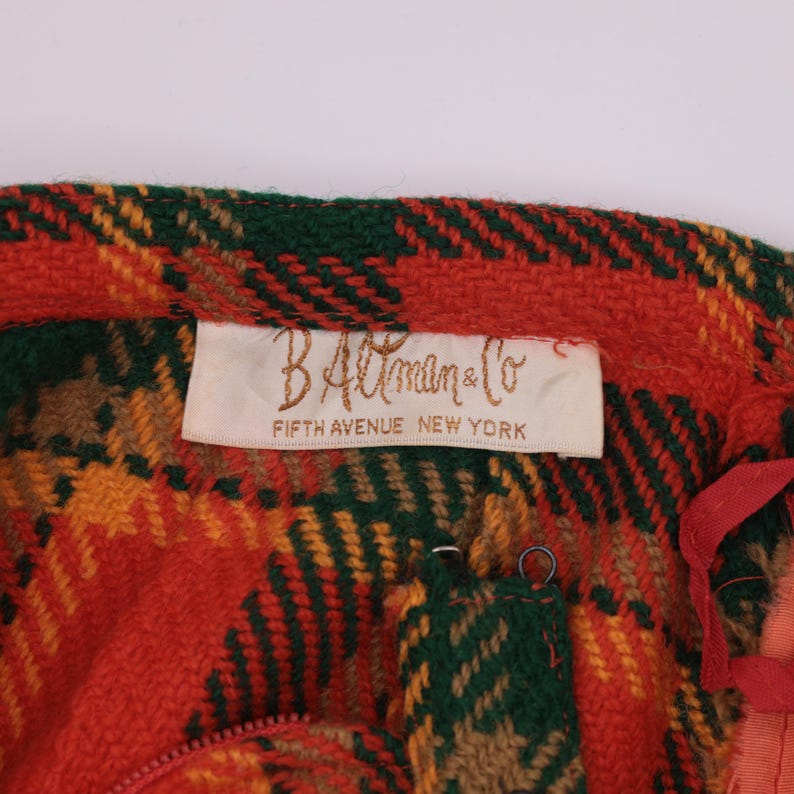 May include: A red, green, and yellow plaid fabric with a white label that reads "B. Altman & Co. Fifth Avenue New York".