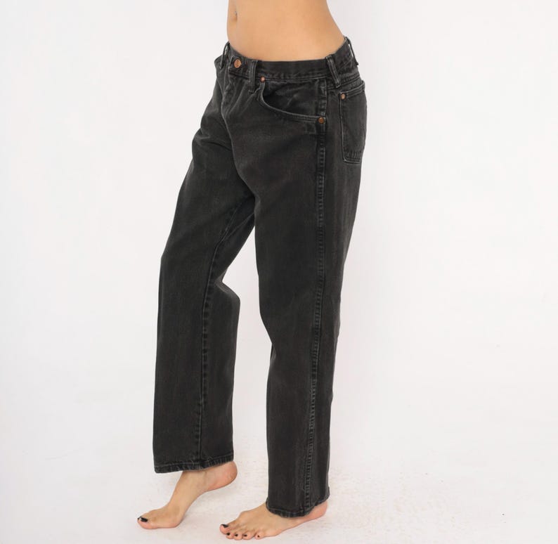 May include: Black denim jeans with a classic five-pocket design. The jeans have a straight leg cut and a faded appearance. The image shows the jeans from the waist down, highlighting the details of the fabric and stitching. The jeans are worn.