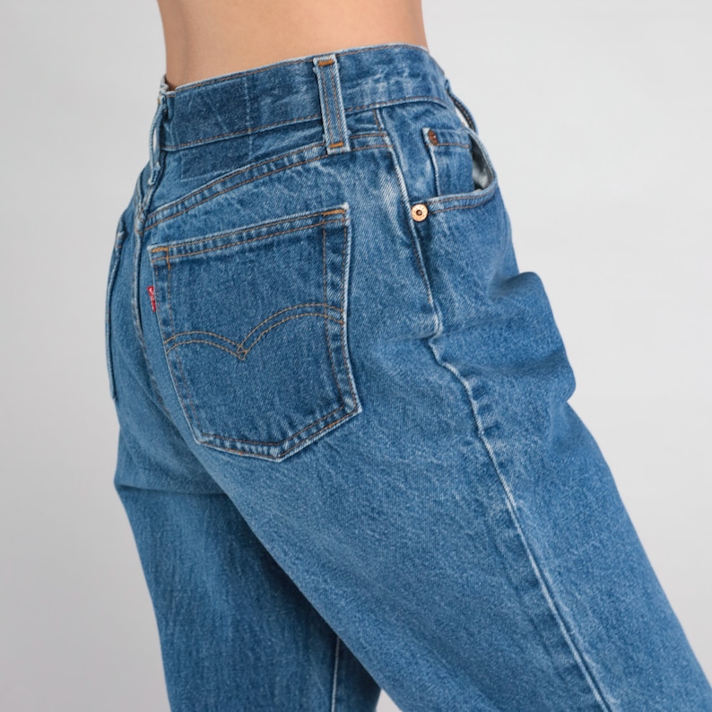 May include: A pair of blue denim jeans with a back pocket and a red tab.