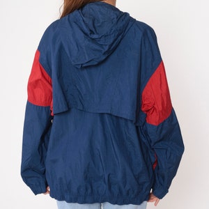 May include: A blue and red hooded windbreaker jacket with a zipper closure. The jacket has a drawstring hood and a contrasting red color on the sleeves and shoulders.
