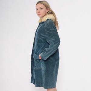 May include: A teal-colored velvet coat with a cream-colored faux fur collar. The coat has a long length, a button closure, and two large front pockets. The coat is a vintage style and appears to be in good condition.