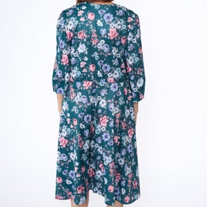 K&ouml;nnte beinhalten: Ein blaues Kleid mit floralem Muster in Rosa, Wei&szlig; und Blau. Das Kleid hat einen V-Ausschnitt und 3/4 &Auml;rmel.