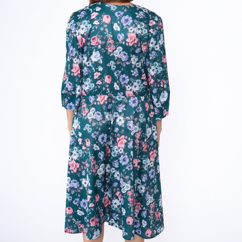 K&ouml;nnte beinhalten: Ein blaues Kleid mit floralem Muster in Rosa, Wei&szlig; und Blau. Das Kleid hat einen V-Ausschnitt und 3/4 &Auml;rmel.