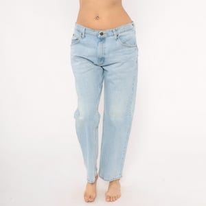 May include: Light blue denim jeans with a classic five-pocket design. The jeans have a straight leg fit and a faded wash, creating a vintage look. The jeans are worn by a person.