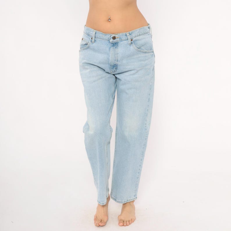 May include: Light blue denim jeans with a classic five-pocket design. The jeans have a straight leg fit and a faded wash, creating a vintage look. The jeans are worn by a person.