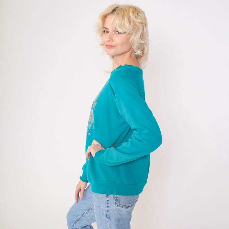 May include: A teal blue sweatshirt with a distressed neckline. The sweatshirt has long sleeves and a relaxed fit.