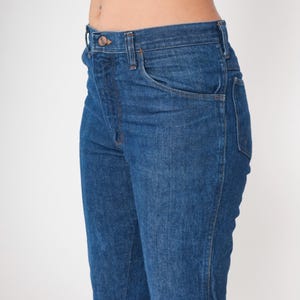 May include: Close-up of blue denim jeans. The jeans have a classic five-pocket design, a button and zipper closure, and a straight leg fit. The denim has a medium wash with subtle fading and a slight sheen.