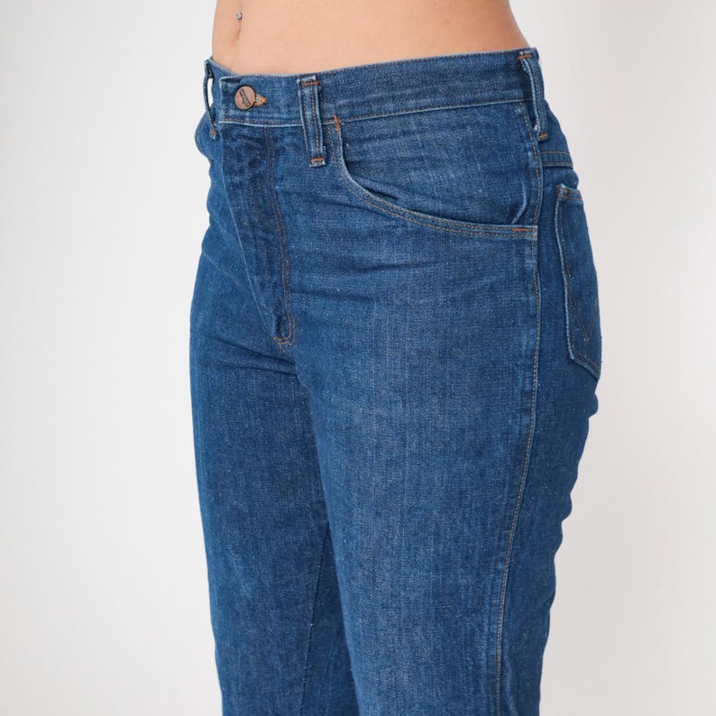 May include: Close-up of blue denim jeans. The jeans have a classic five-pocket design, a button and zipper closure, and a straight leg fit. The denim has a medium wash with subtle fading and a slight sheen.