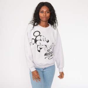 May include: A gray sweatshirt with a black and white graphic of Mickey Mouse. The graphic shows Mickey Mouse with his signature grin and a black signature that says "Mickey" underneath.