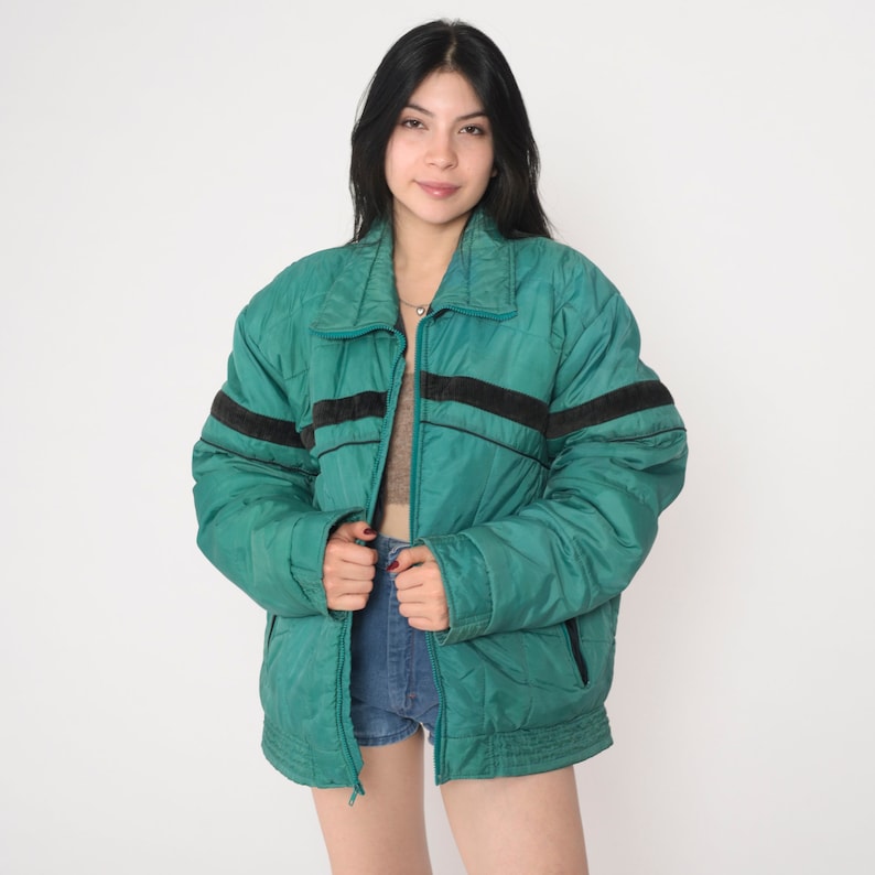 May include: A teal blue puffer jacket with black and white stripes on the sleeves. The jacket has a zipper closure and a stand-up collar.