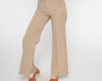 Puede incluir: Pantalones color beige de cintura alta con pernera ancha. Los pantalones tienen un aspecto limpio y entallado con una cinturilla sencilla. La modelo lleva tacones abiertos marrones. Los pantalones son de tejido liso y liso.