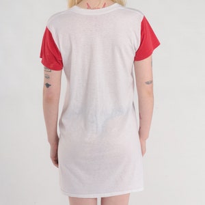 K&ouml;nnte beinhalten: Wei&szlig;es T-Shirt-Kleid mit roten &Auml;rmeln. Das Kleid hat eine lockere Passform und einen runden Ausschnitt.