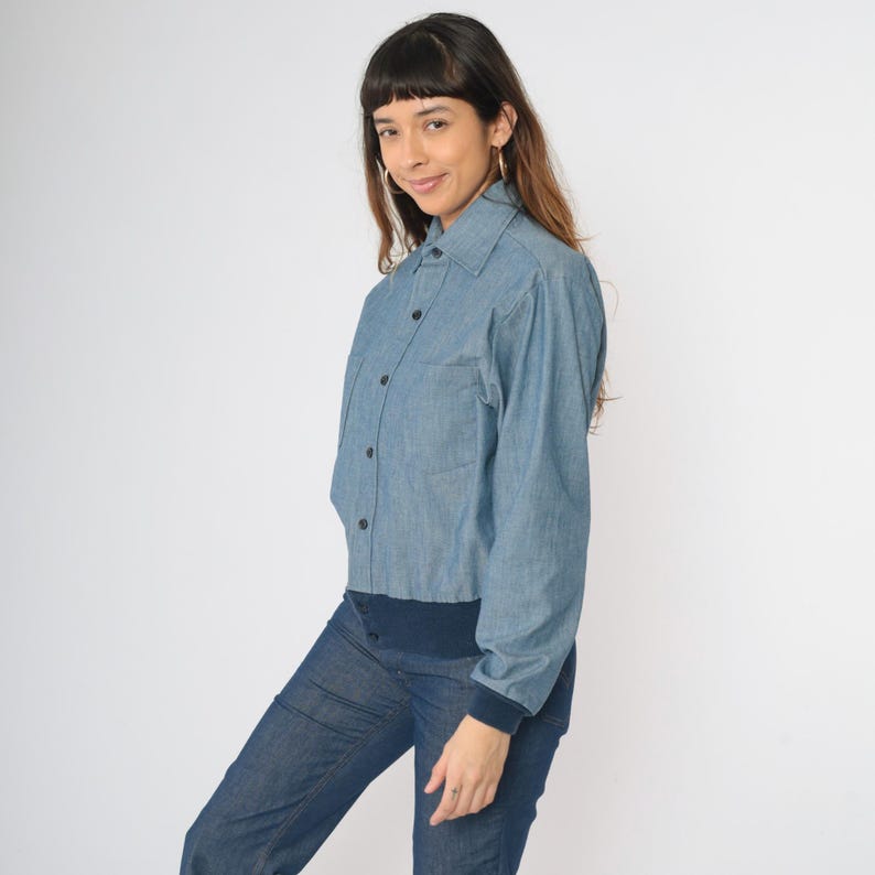 May include: A light blue denim shirt with a button-up front and long sleeves. The shirt has a collar and a single chest pocket.