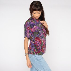 May include: A purple, pink, and green floral print short-sleeved shirt with a mock neck.