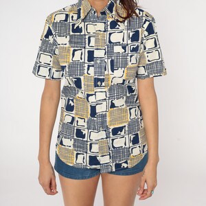 May include: A short-sleeved button-down shirt with a geometric pattern in shades of blue and yellow on a white background.