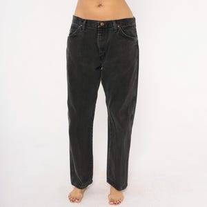 May include: Black denim jeans with a classic five-pocket design. The jeans have a button and zipper closure and a straight leg fit. The dark wash denim is slightly faded, giving them a vintage look. The jeans are shown on a white background.