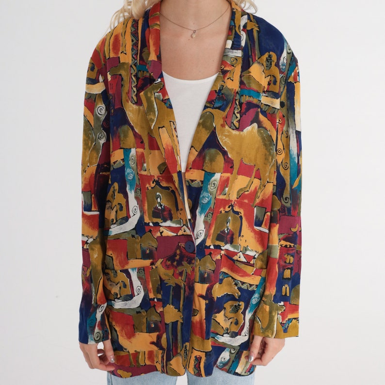 May include: A colorful blazer with an abstract pattern featuring camel figures, geometric shapes, and various colors including yellow, red, blue, and green. The blazer has a wide lapel and a single button closure.