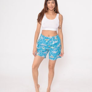 K&ouml;nnte beinhalten: Blaue Badeshorts mit einem bunten Aufdruck von Surfern, Booten und Fischen. Die Shorts haben einen Kordelzugbund und sind aus einem leichten Stoff.