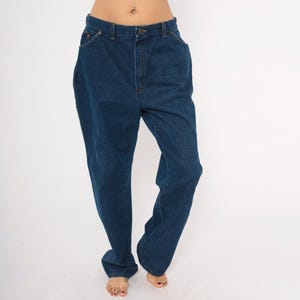 May include: Dark blue denim jeans with a classic five-pocket design. The jeans have a straight leg cut and a button and zipper closure. The fabric appears to be a medium-weight denim. The jeans are shown on a white background.