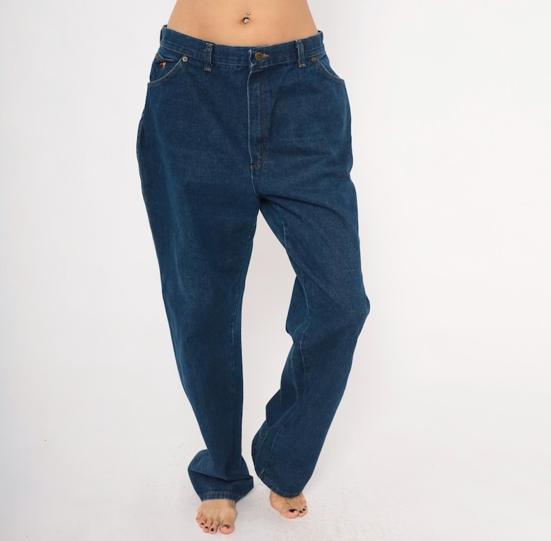 May include: Dark blue denim jeans with a classic five-pocket design. The jeans have a straight leg cut and a button and zipper closure. The fabric appears to be a medium-weight denim. The jeans are shown on a white background.