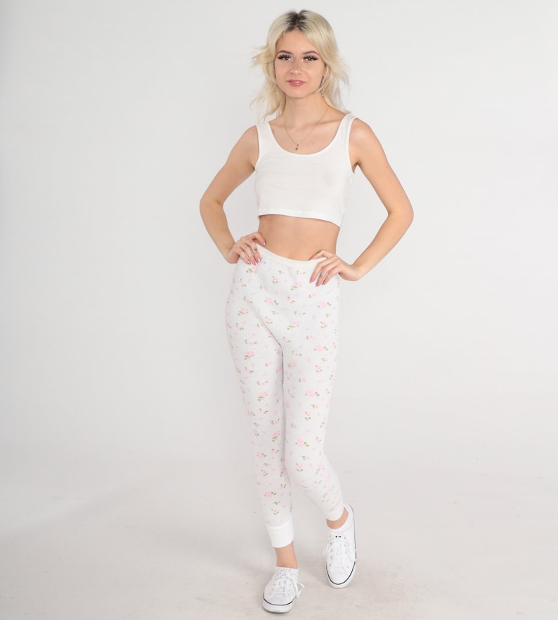 May include: A woman wearing a white tank top and white floral print leggings with white sneakers.