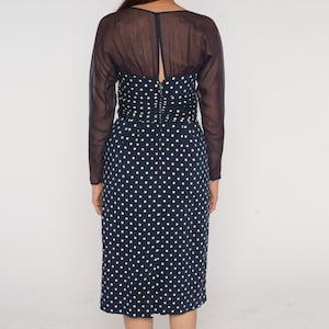 May include: A navy blue midi dress with white polka dots and a sheer black overlay. The dress has a fitted bodice and a slightly flared skirt.