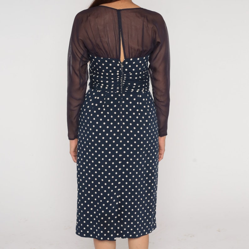 May include: A navy blue midi dress with white polka dots and a sheer black overlay. The dress has a fitted bodice and a slightly flared skirt.